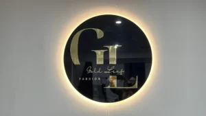 Round black backlit logo sign with a gold monogram on a white wall