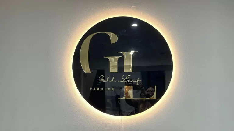 Round black backlit logo sign with a gold monogram on a white wall