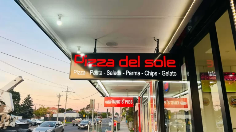 Illuminated Piazza del Sole shopfront sign under a street awning
